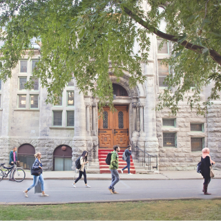 Students walking on campus in the summer in front of a stone building