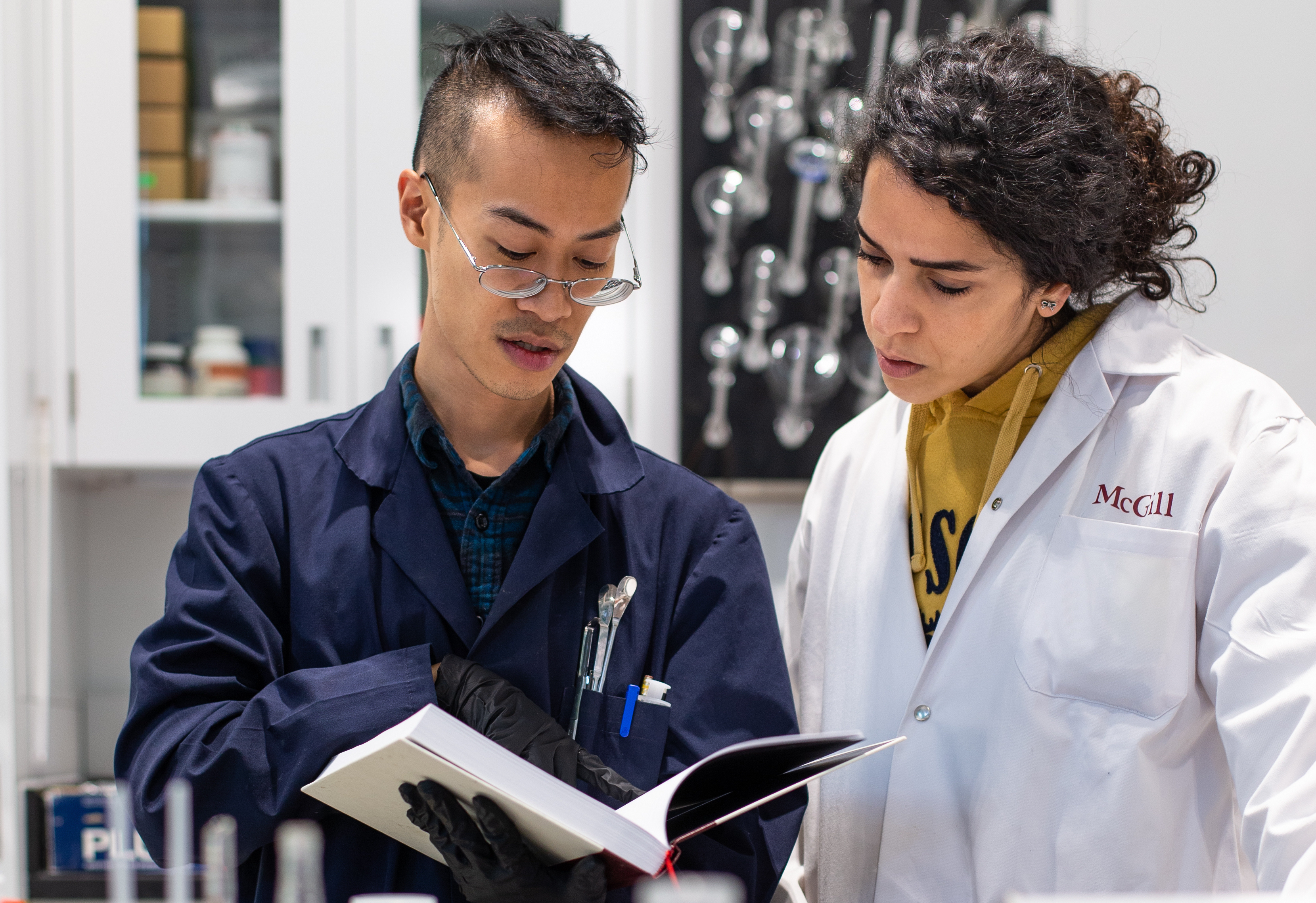 Two students in a lab looking at the contents of a textbook.