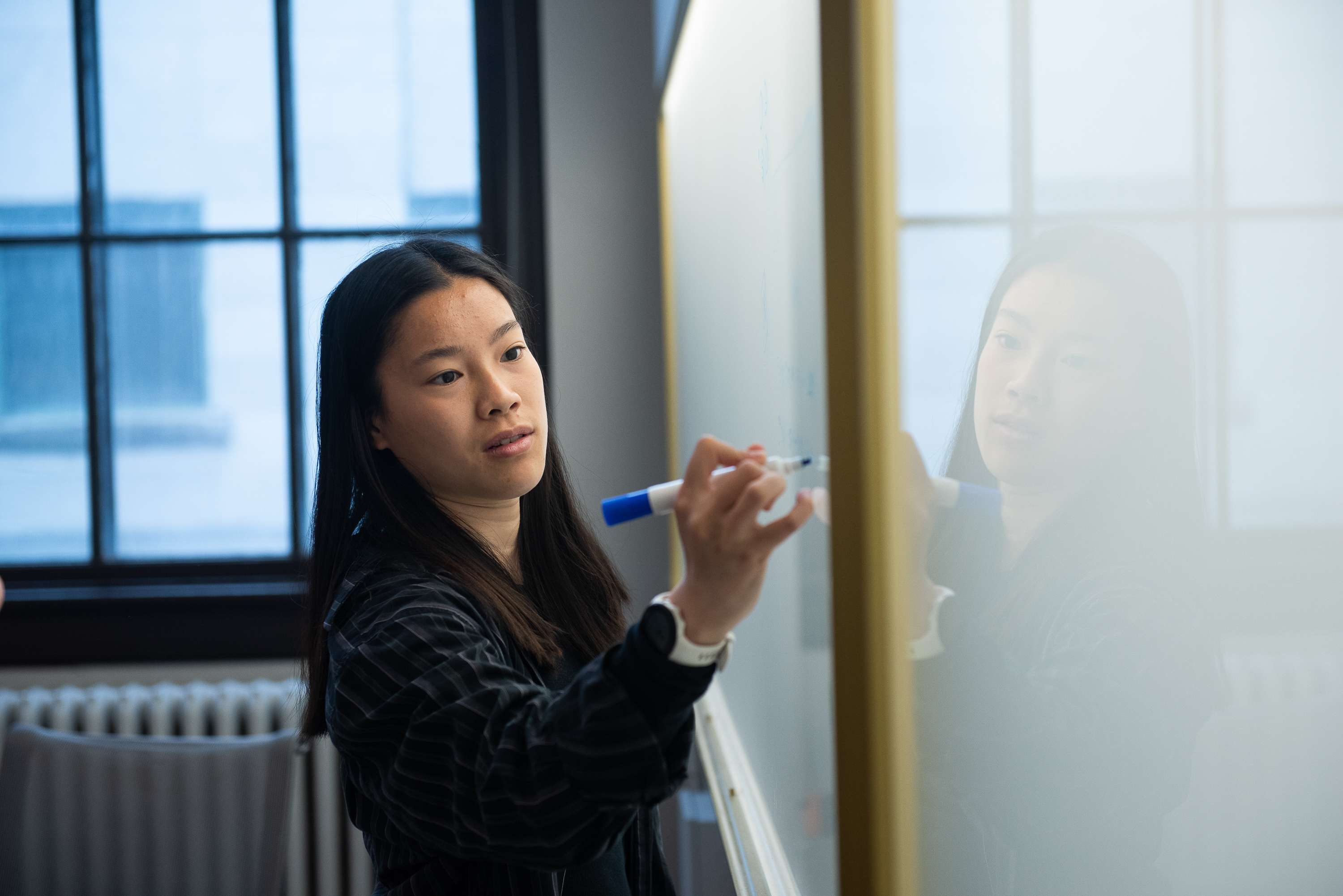 a woman writing on a white board with a blue marker