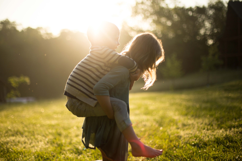 Woman carrying a child on her back in a sunny field