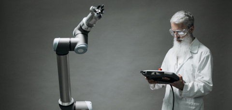 A man with a beard and lab coat facing a robotic arm