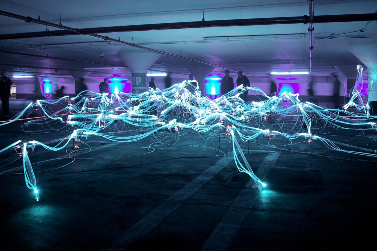 A network of lit up wires glowing in the dark in an indoor parking lot.