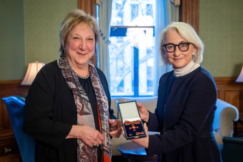 Ambassador Sparwasser handing Martha Crago the Order of Merit medal and smiling at the camera
