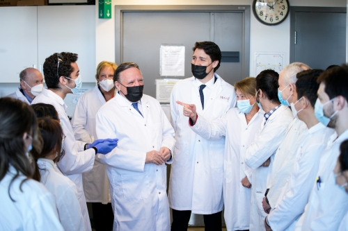 Prime Minister Trudeau and Quebec Premier Francois Legault, wearing laboratory coats with a group of people. 