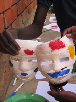 Child holding a hand-made mask. The mask is made from plaster and painted in colours blue, red, and yellow. 