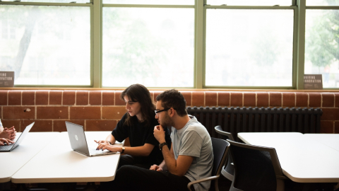 Woman and man sit at a table and look at the screen of a laptop