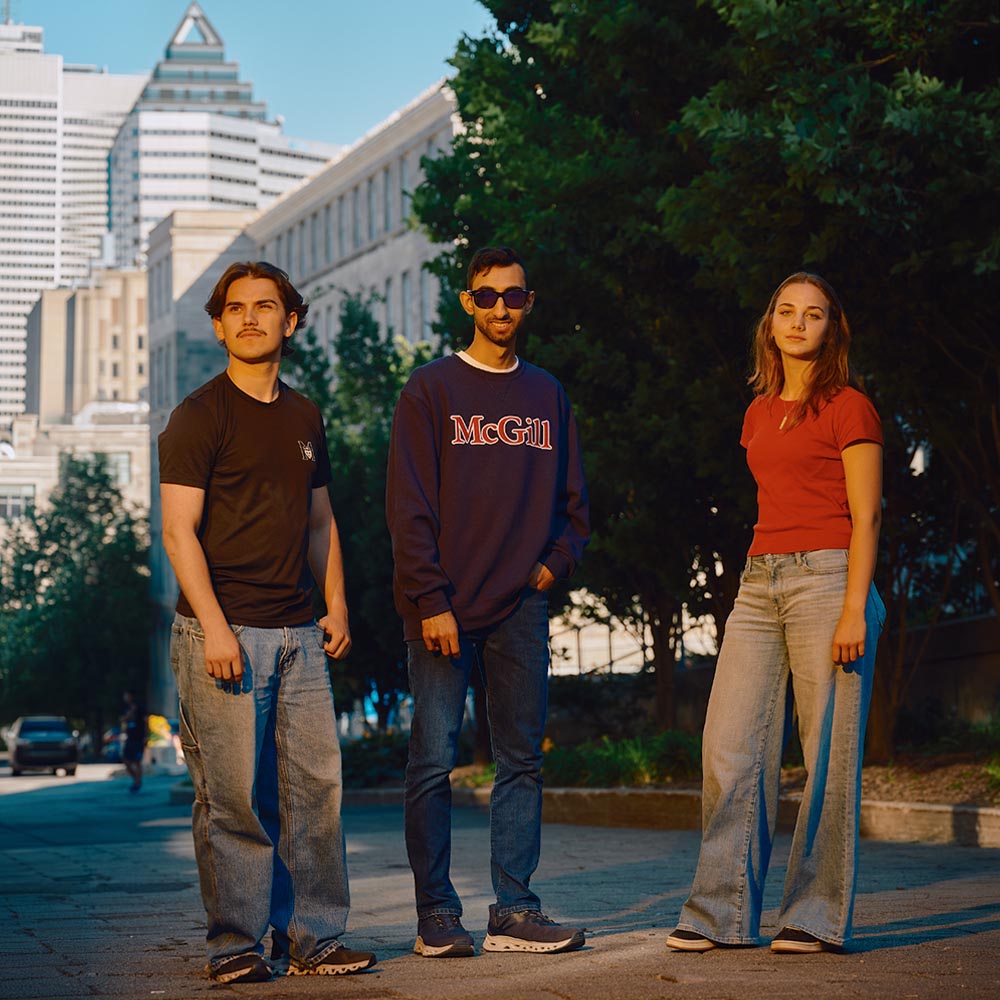 Trois étudiants se tiennent à l’extérieur sur le campus de McGill, portant des chandails à l’effigie de McGill et des jeans.
