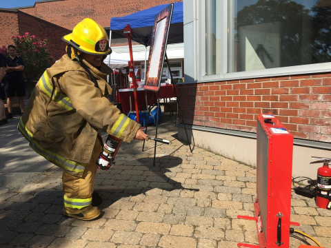 Student using fire extinguisher simulator while dressed in firefighter suit