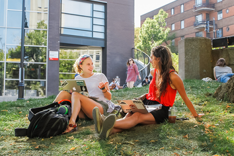 Two female students sitting on the grass on campus grounds