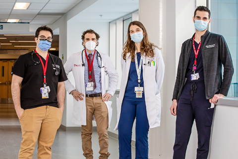 Quatre médecins résidents portant des masques chirurgicaux debout dans un corridor d'hôpital