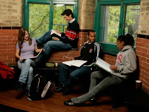 Four students studying together while sitting in a corner of a brick building