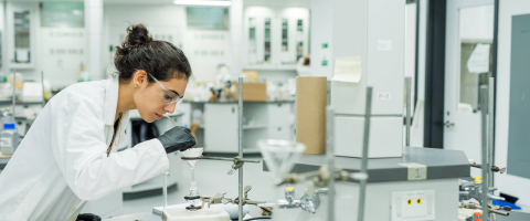 Woman in a white lab coat looking through a microscope in a laboratory