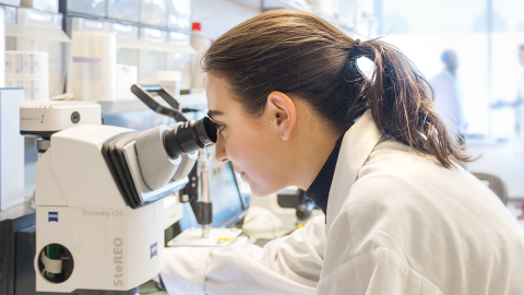 Woman in a white lab coat looking through a microscope in a laboratory