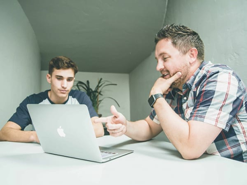 Person with laptop sitting at white desk talking to the student sitting on the other side