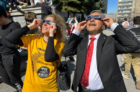 Two people with eclipse glasses on, smiling, looking up at the sky. 
