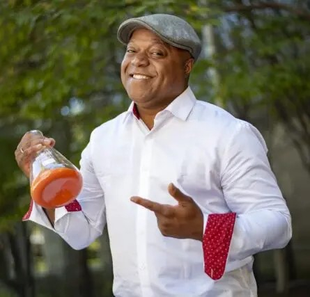 Frederic Bertley smiling and holding an Erlenmeyer flask containing an orange substance.