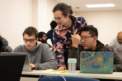 Three young adults discussing their work behind laptops at the McGill Physics Hackathon.