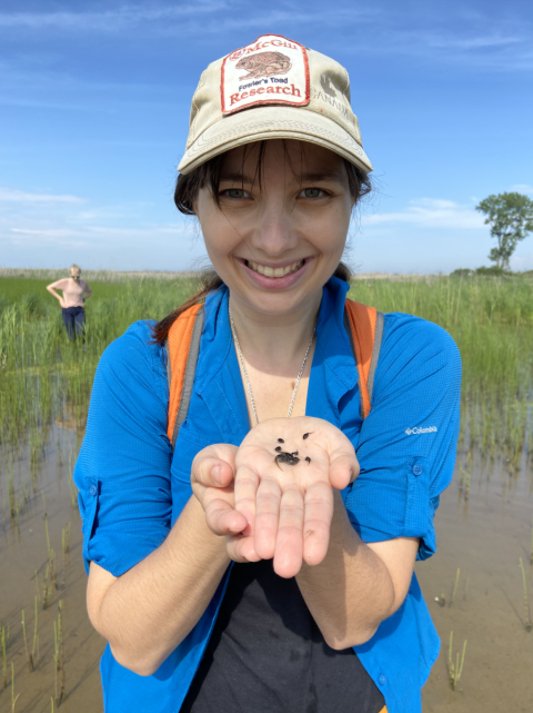 A front facing photo of Jessica Ford in the field, holding tadpoles up to the camera.
