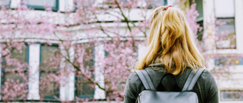 Girl with backpack looking at blossoms.