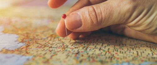 A hand putting a red pin on a large map