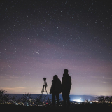 Deux personnes avec un télescope regardant le ciel nocturne.