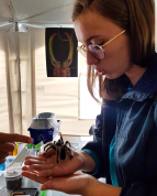 Une femme dans un labo avec une grande araignéé sur la paume de sa main