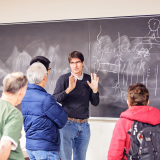 A man stands in front of a board explaining a concept. 