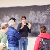 A man stands in front of a blackboard with 4 people