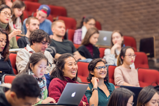 Students are laughing while they are sitting in a lecture hall. 