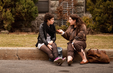 two young women, sitting on a curb having a conversation