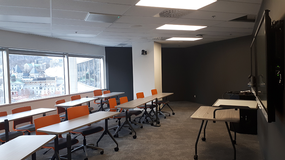 Room 1135 at 2001 McGill College - Classroom with orange desk chairs in front of long tables with a window to the McGill campus