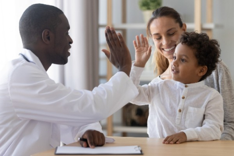 A male doctor high-fives a young boy who is sitting on this mother's lap