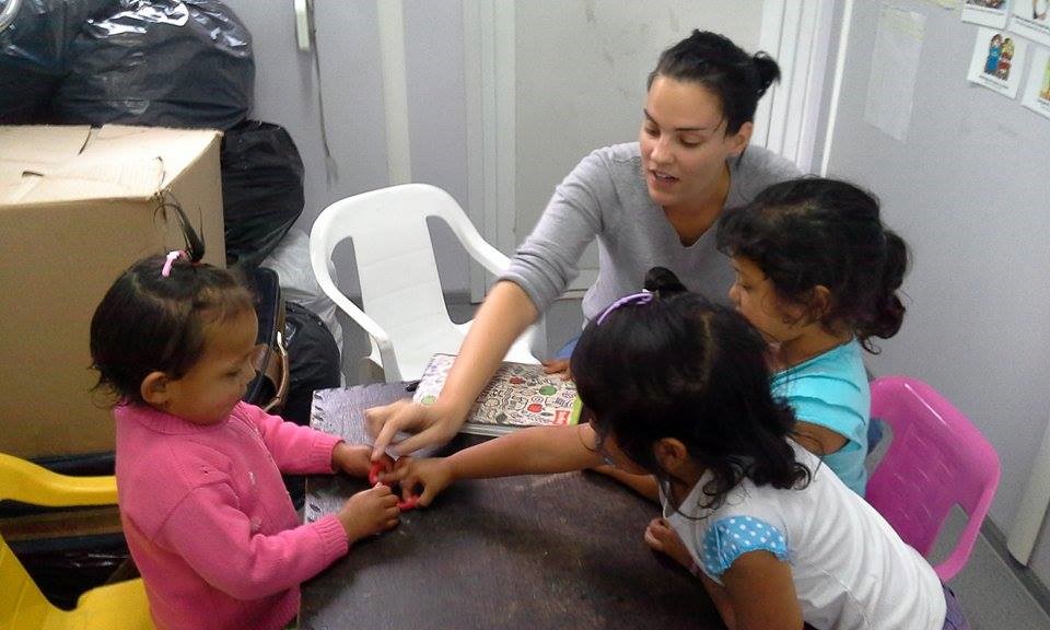 Female university student helping children at a classroom table. 