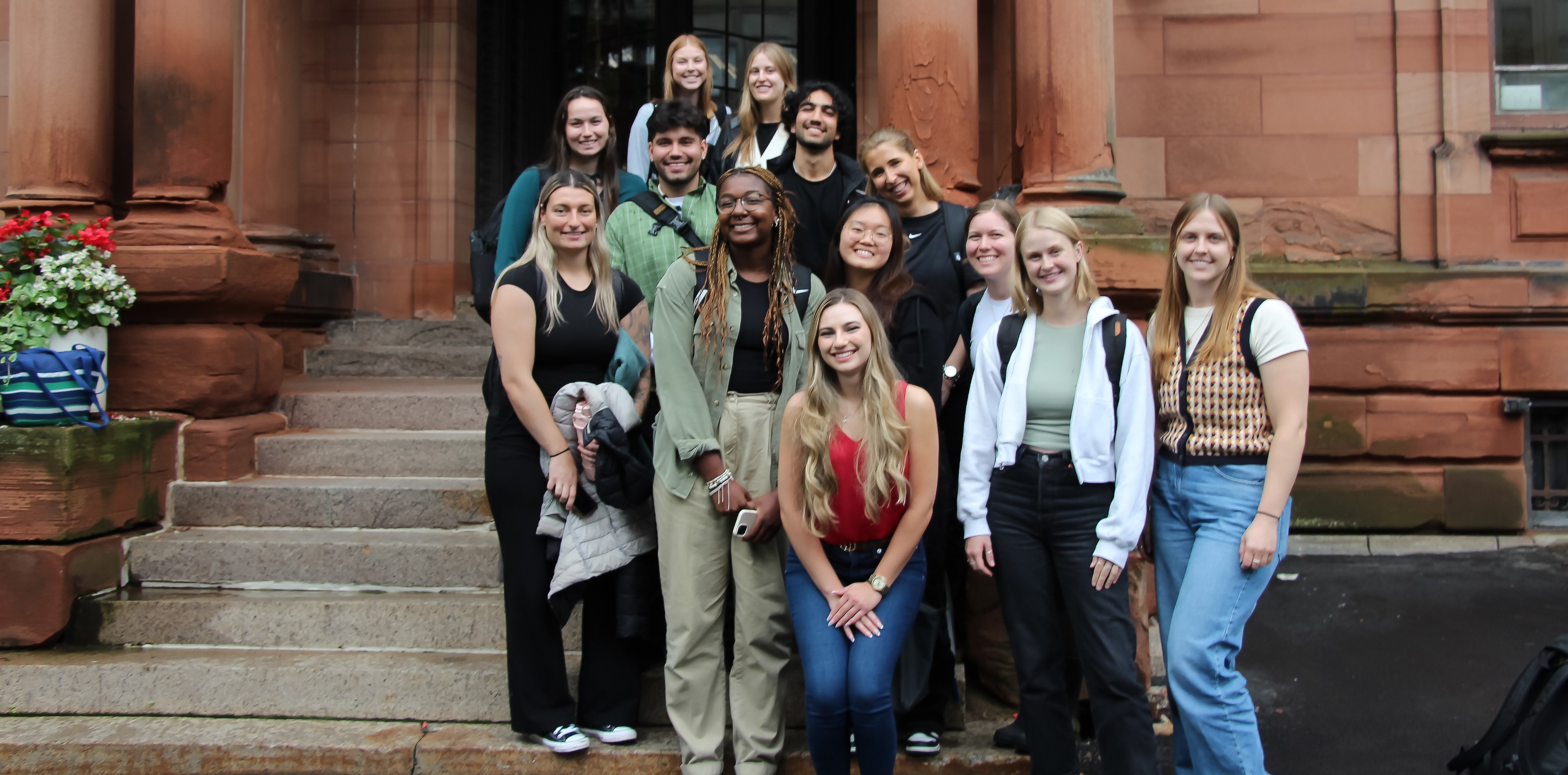 A diverse group of 13 OT students standing in front of Hosmer Building 