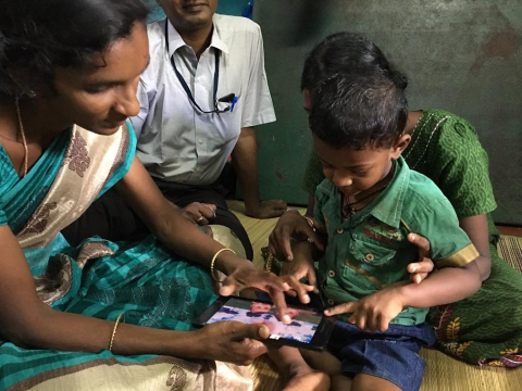 Healthcare worker in India interacting with young child and an ipad. 