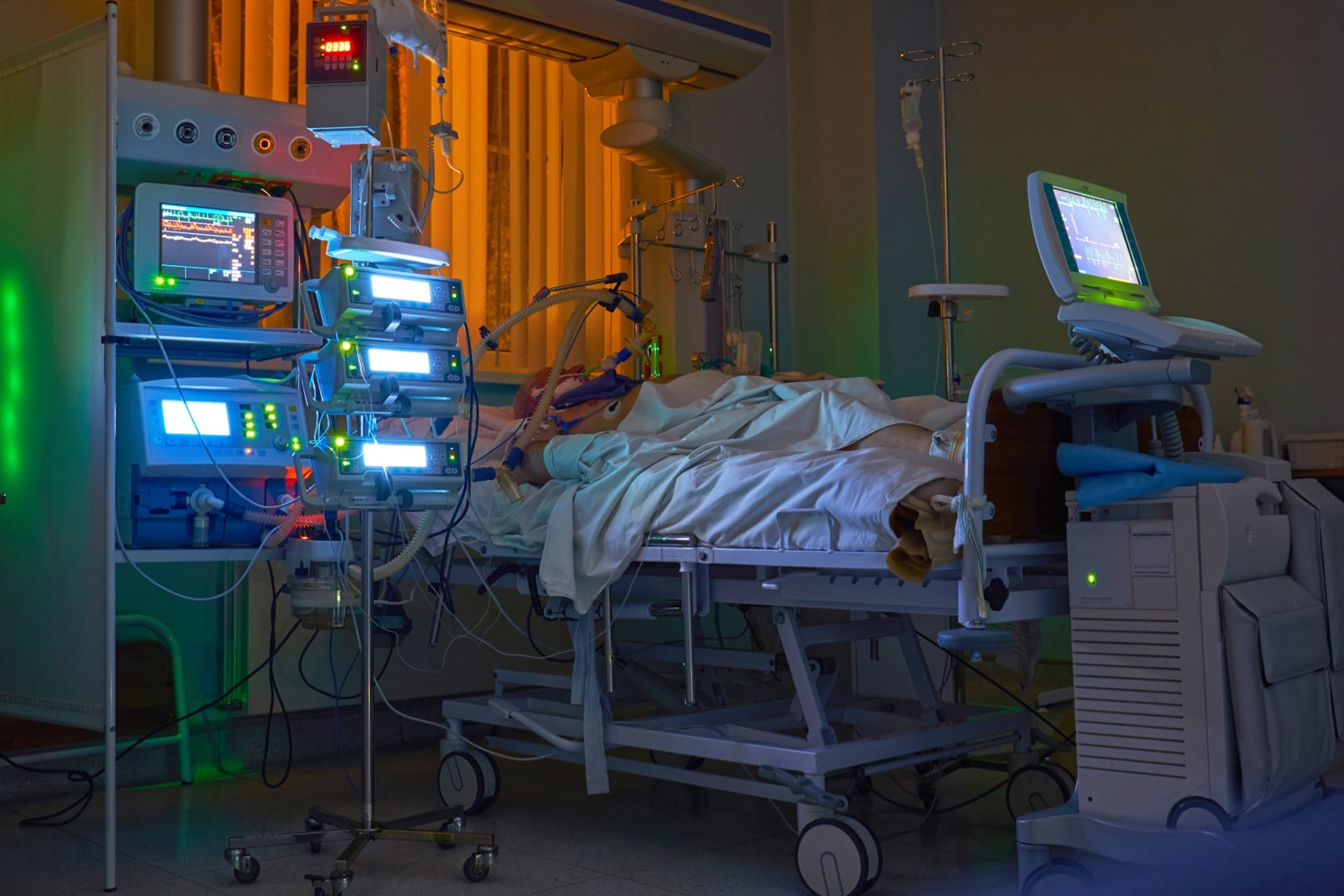 ICU room with glowing lights of monitors surrounding patient lying in bed