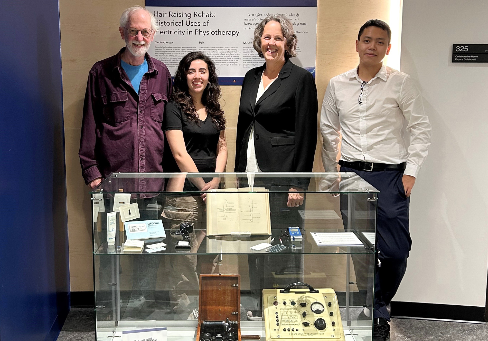 Dr Rick Fraser, Nadia Bichri, Sarah Marshall and Daniel Lee, smiling and standing behind display case of antique equipment
