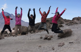 Five students jumping with mountains in the background 