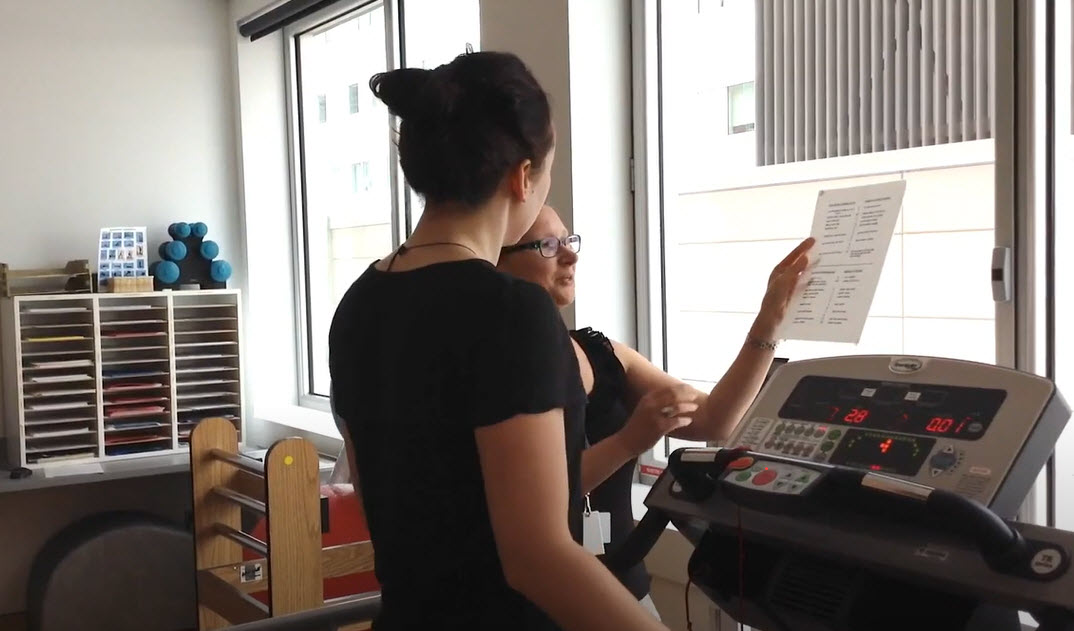 Researcher explaining information to a young participant who is on a treadmill 