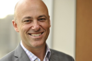 Head shot of Alain, a white man, with the collar of a white shirt and gray jacket showing. He is smiling widely.