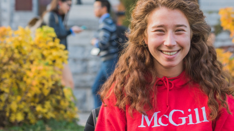smiling student sitting on campus wearing a McGill sweater