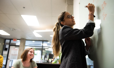 A workshop facilitator writes on a whiteboard while a student looks on