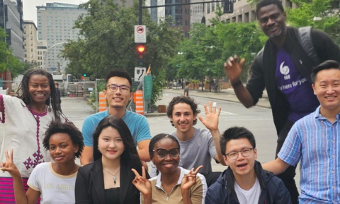 A group of 9 international students smiles for a photo outside on Sherbrooke street