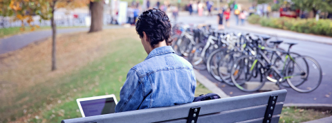 a student sitting on a bench alone on his laptop