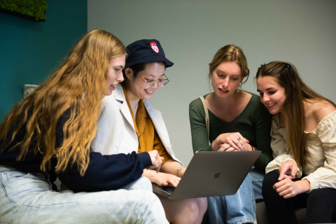 4 students seated in the Student Wellness Hub looking at a laptop