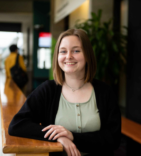 A student smiles as she leans on the railing of a hallway in Brown Student Services Building