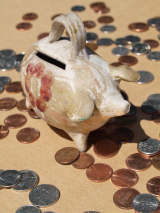 a ceramic piggy bank stands on a table with coins strewn around it 