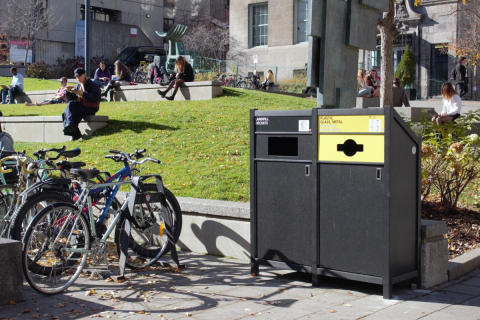 Landfill and plastic/metal recycling bins are pictured on the McGill campus next to bike racks and green space.