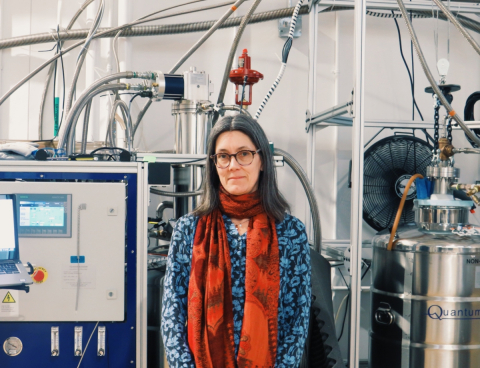 A woman looks into the camera standing in front of part of a helium recovery system.