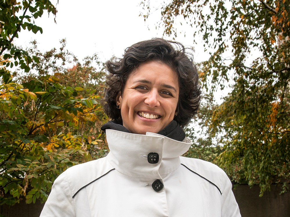A woman in a white jacket smiles outside 